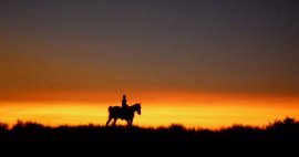 Native American youth seen in silhouette on horseback against a orange-hued sunset