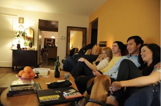 Two couples sit on couch watching TV with dog watching them